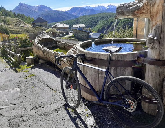 velo gravel posé contre une fontaine sous le ciel bleu du Queyras