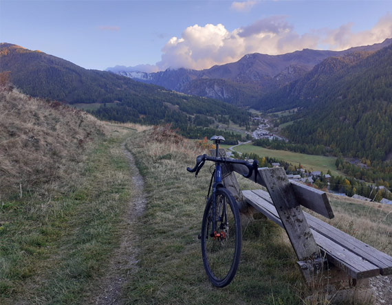 vélo gravel posé contre un banc devant les vallées du Queyras